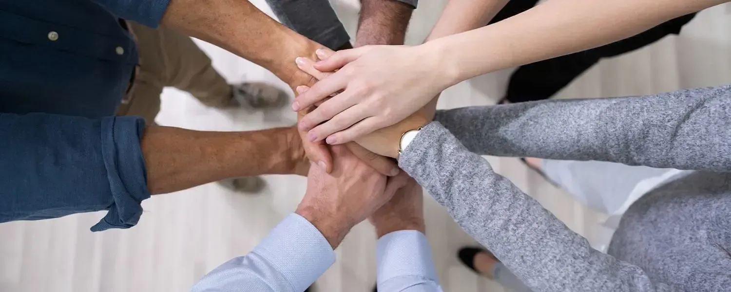 Several people stack their hands on top of one another in a circle, seen from above.