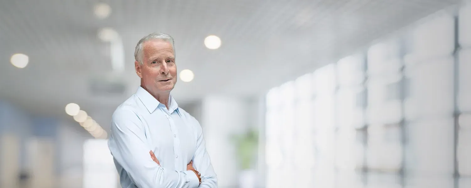 Portrait of a grey-haired man in a light shirt, arms folded, in a bright hospital corridor (photo montage).