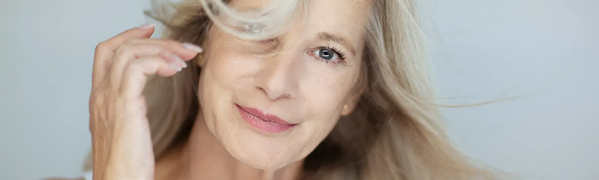 Portrait of a smiling woman with long, light blonde hair, brushing a strand away from her face.