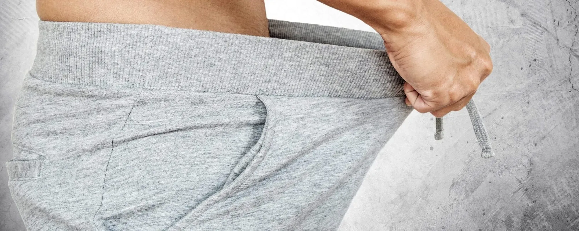 A man pulling the waistband of his grey jogging trousers forward and looking down.
