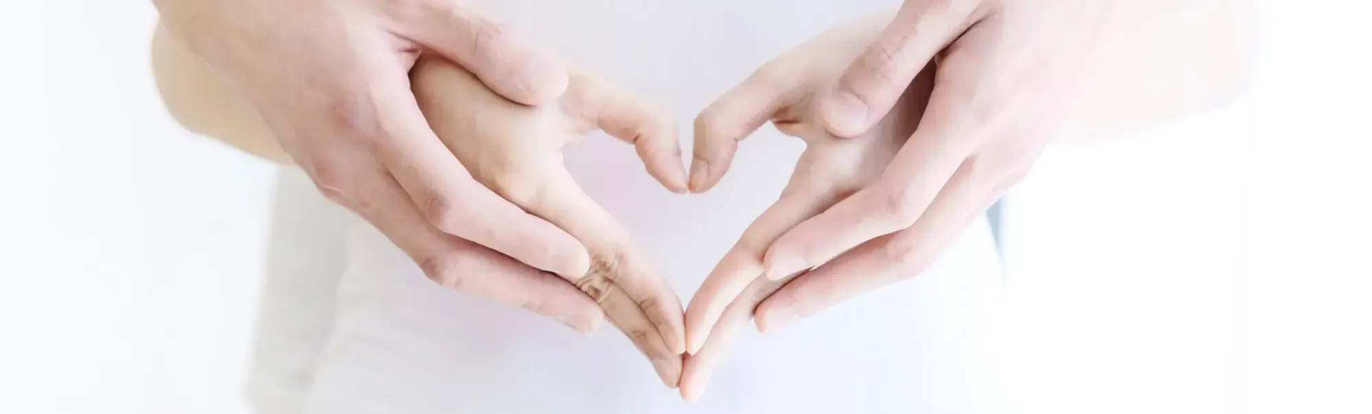 Two pairs of hands forming a heart in front of a white shirt.