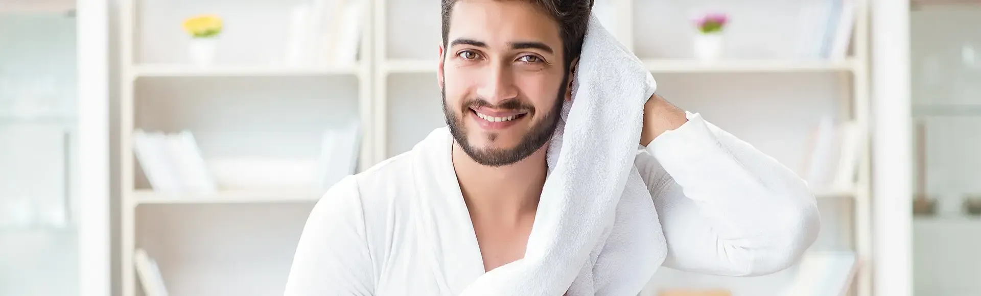 A smiling man in a white bathrobe drying his hair with a white towel.
